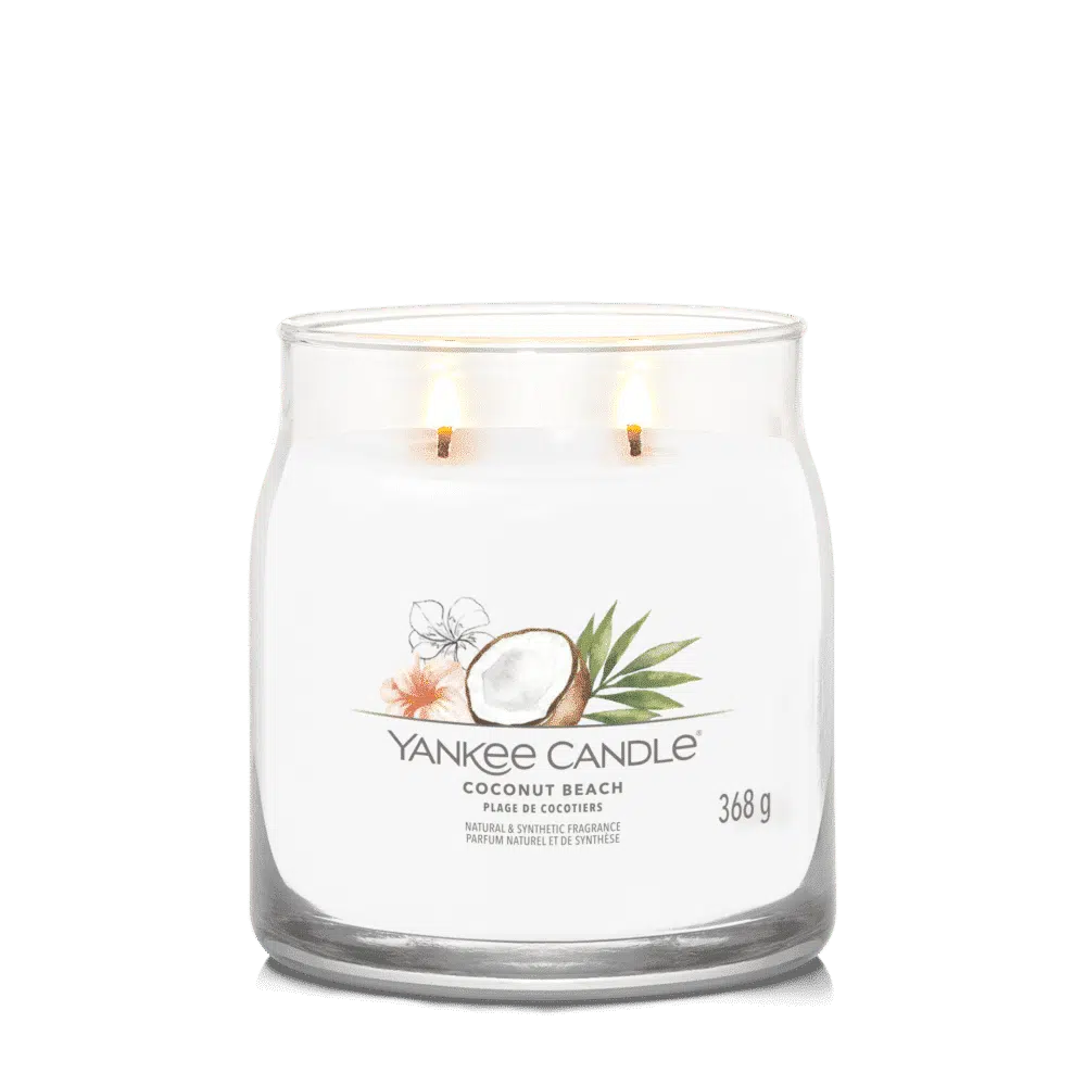 A white Yankee Candle with coconut beach scent and two lit wicks.