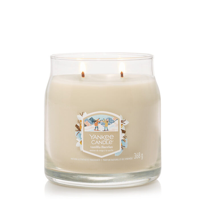 Doftljus med vanilj i glasburk, två brinnande vaxljus.