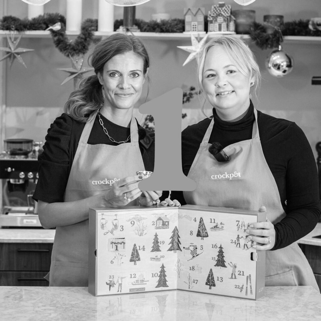 Två personer med förkläden och en adventskalender i ett julpyntat kök.