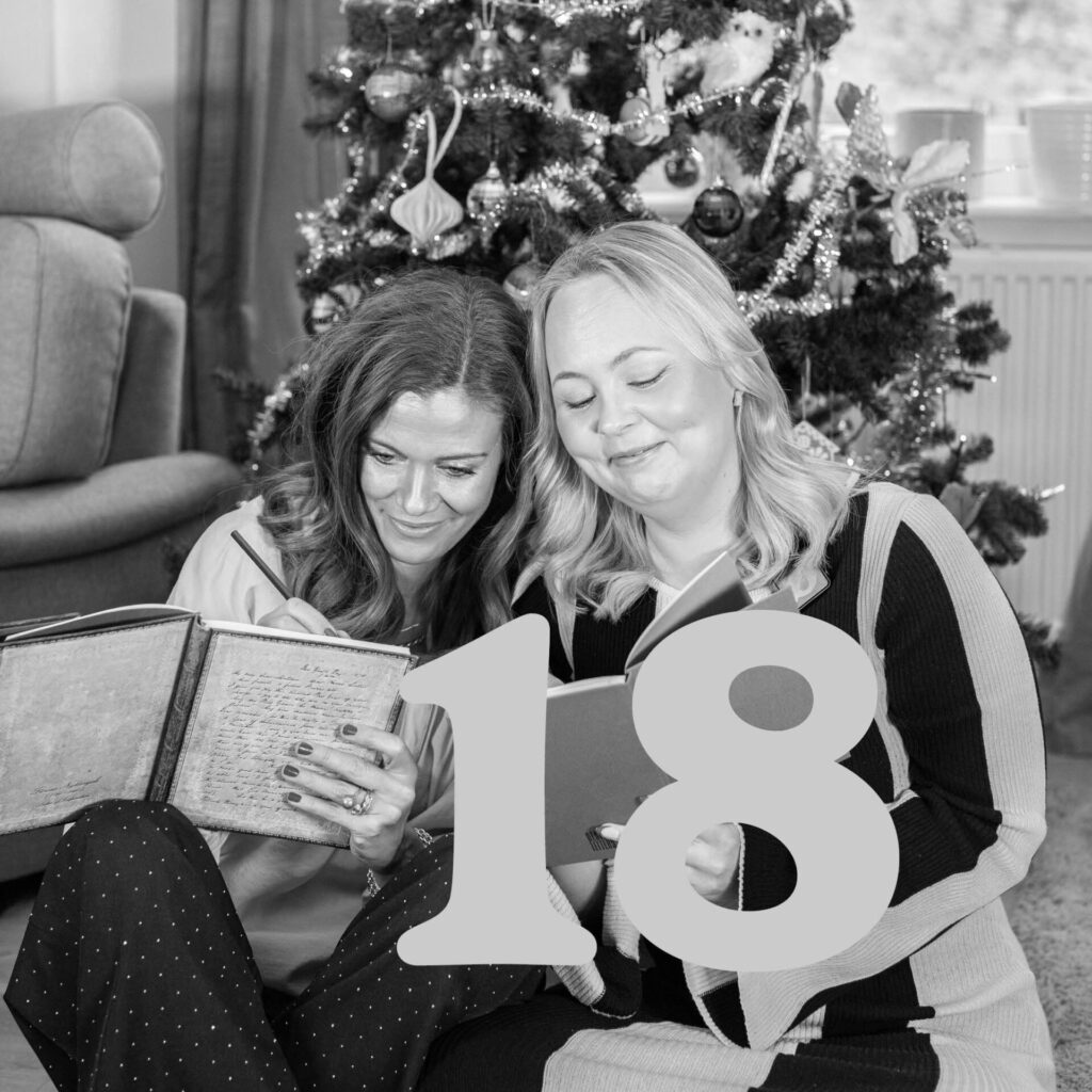 Två kvinnor läser anteckningsböcker framför en julgran, siffra 18 i förgrunden.