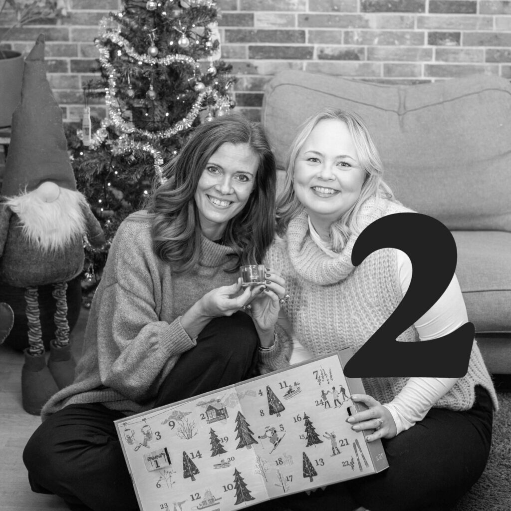 Två kvinnor firar advent med kalendergåva framför dekorerad julgran.