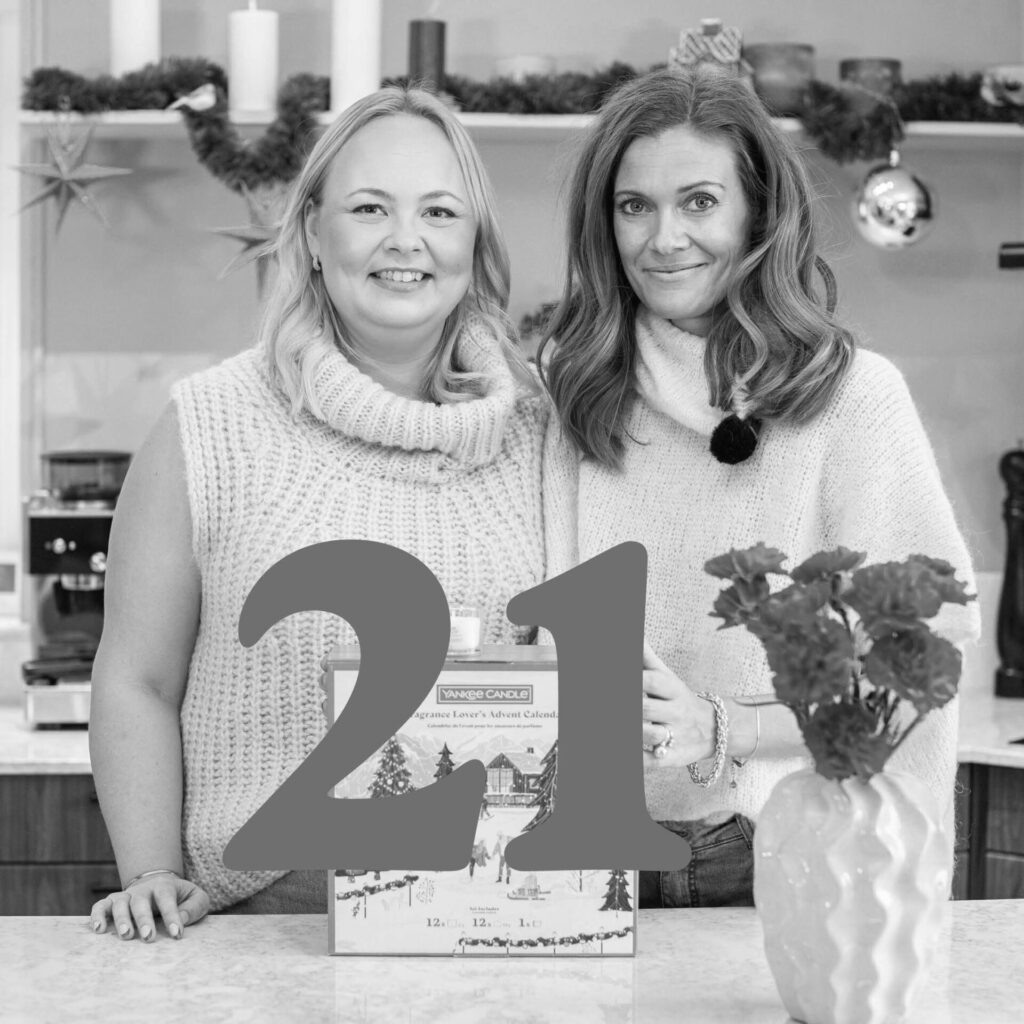 Två kvinnor med stickade tröjor firar jul vid adventskalender.