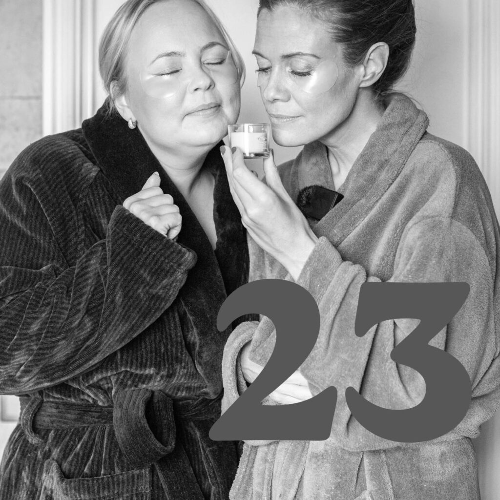 Två kvinnor i morgonrockar och ansiktsmask njuter av ett doftljus, nummer 23.