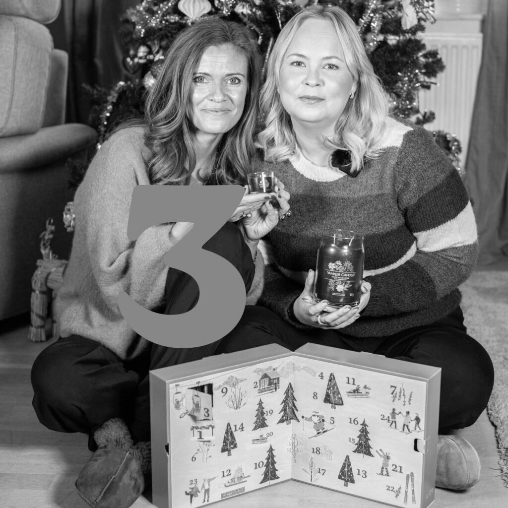 Två personer med adventskalender och doftljus framför julgran.