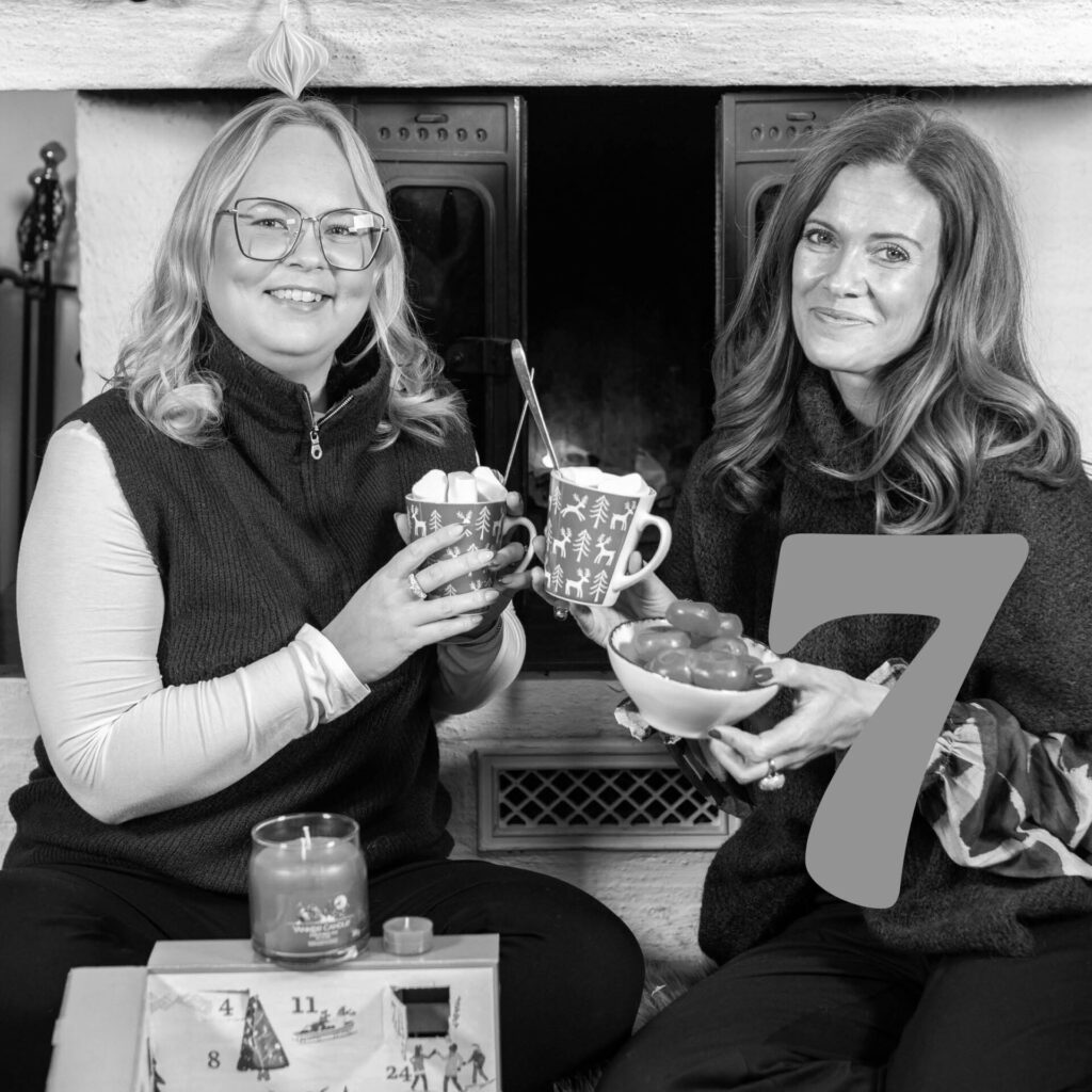 Två leende kvinnor vid en eldplats med varm choklad och nummer sju.