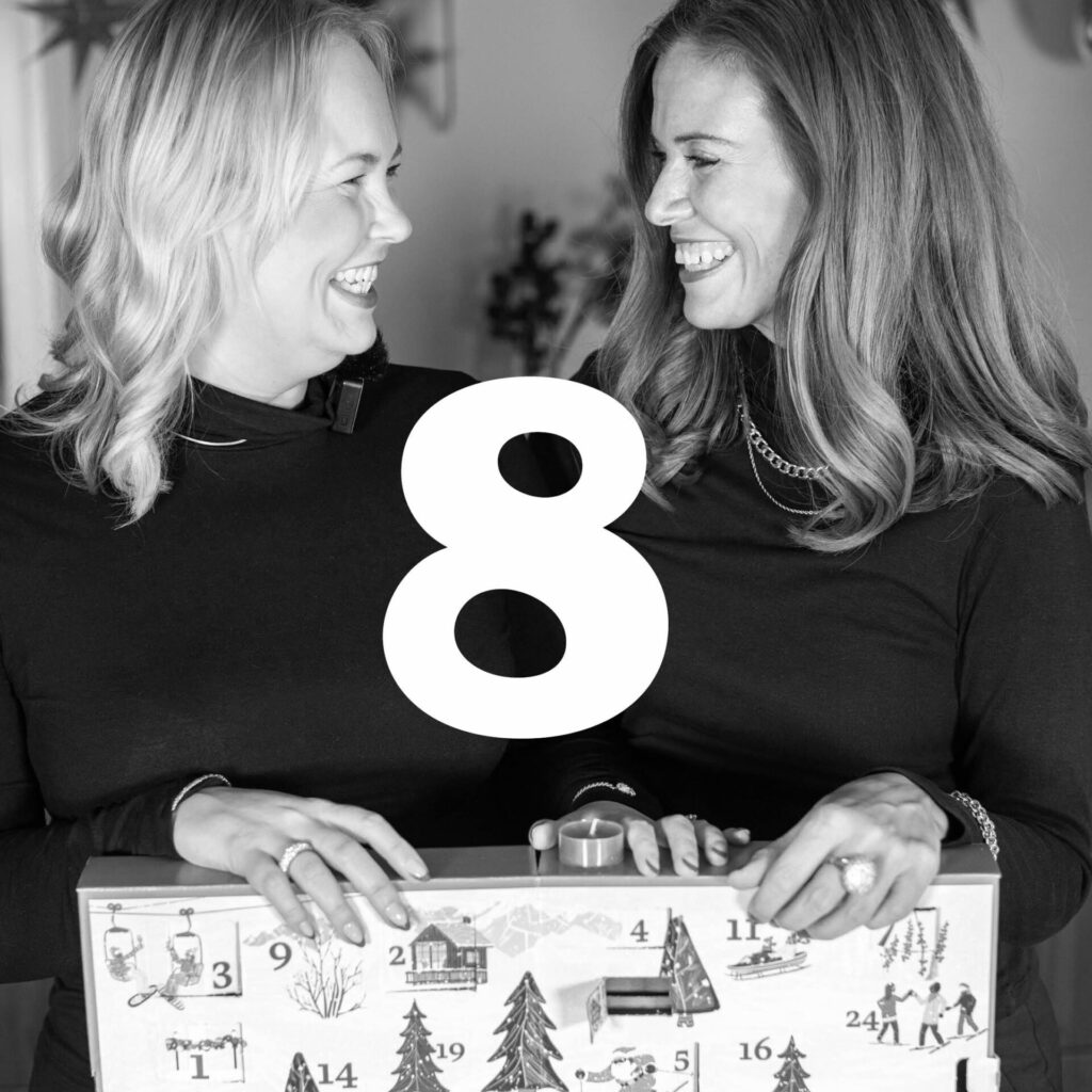 Två leende kvinnor med adventskalender i svartvitt, nummer åtta syns stort i bilden.