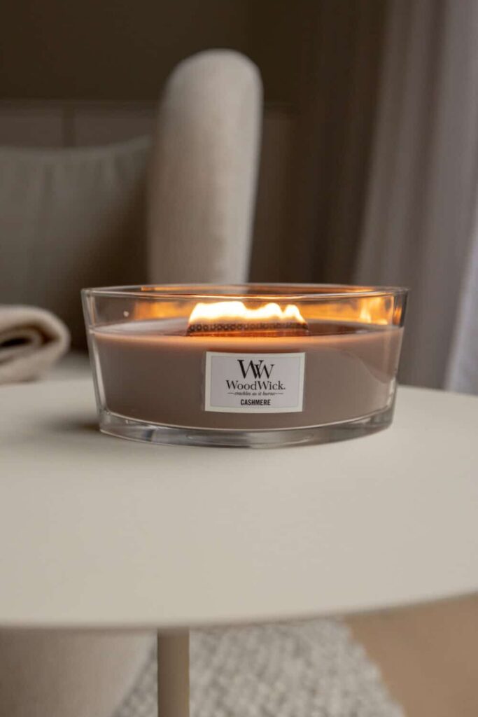 Doftljus från WoodWick i glasburk på bord, skapar mysigt sken.